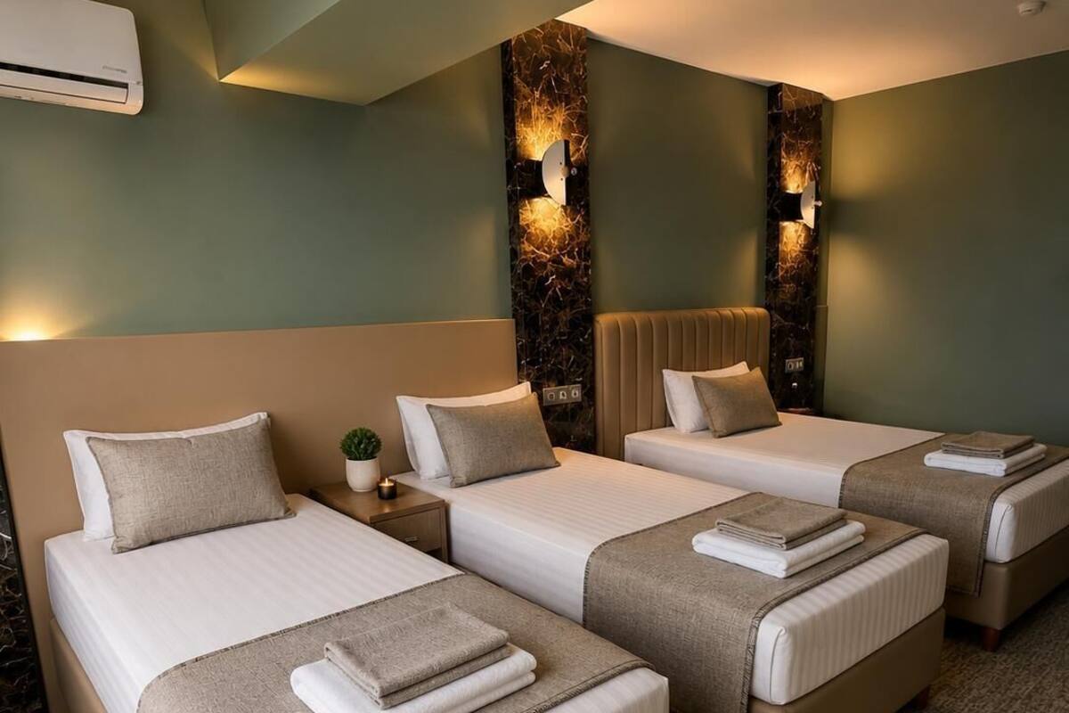 Una habitación de hotel con tres camas, aire acondicionado de pared y luces decorativas en la pared.