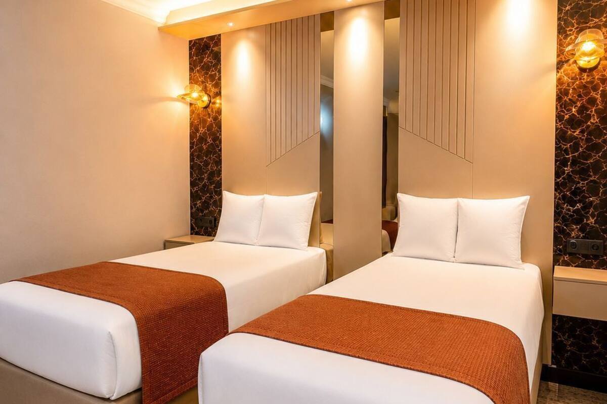 Habitación de hotel con dos camas, piso alfombrado y pared con diseño texturizado.