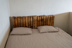 Un lit avec une tête de lit en bois, deux oreillers et un mur uni.