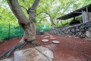 Un sendero de piedra que conduce a un espacio cubierto con un muro de piedra y un árbol.