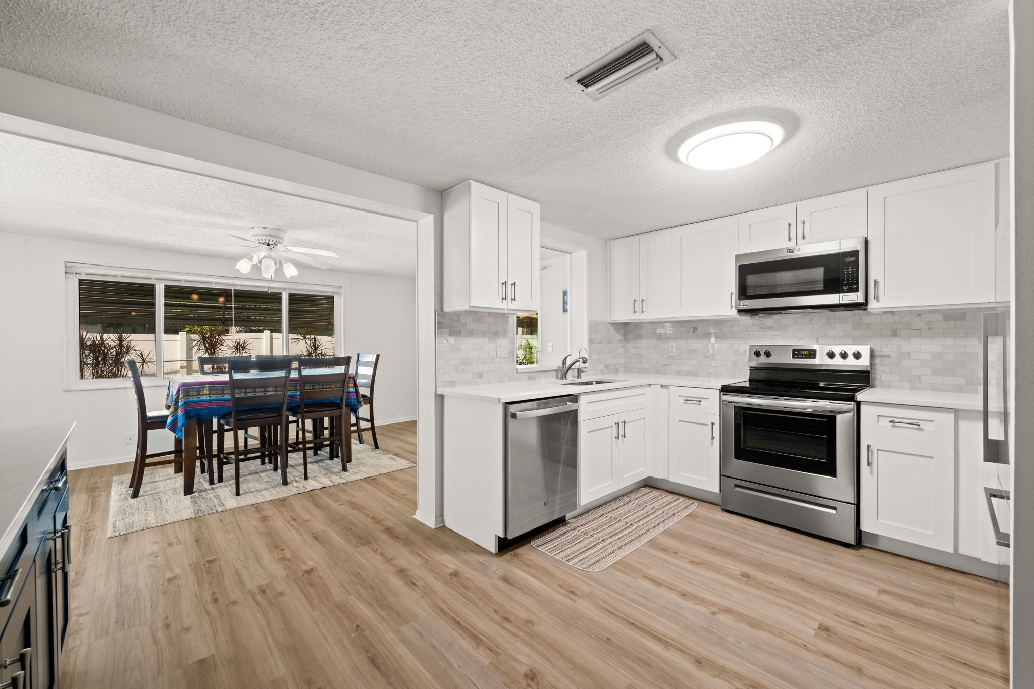 A modern kitchen with white cabinets, stainless steel appliances, and a dining area with a table and chairs.