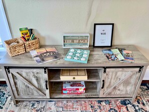 A wooden console table with a framed welcome sign, a framed WiFi sign, travel magazines, and a box of crayons. - Adorable In Aqua Cottage (Galveston)