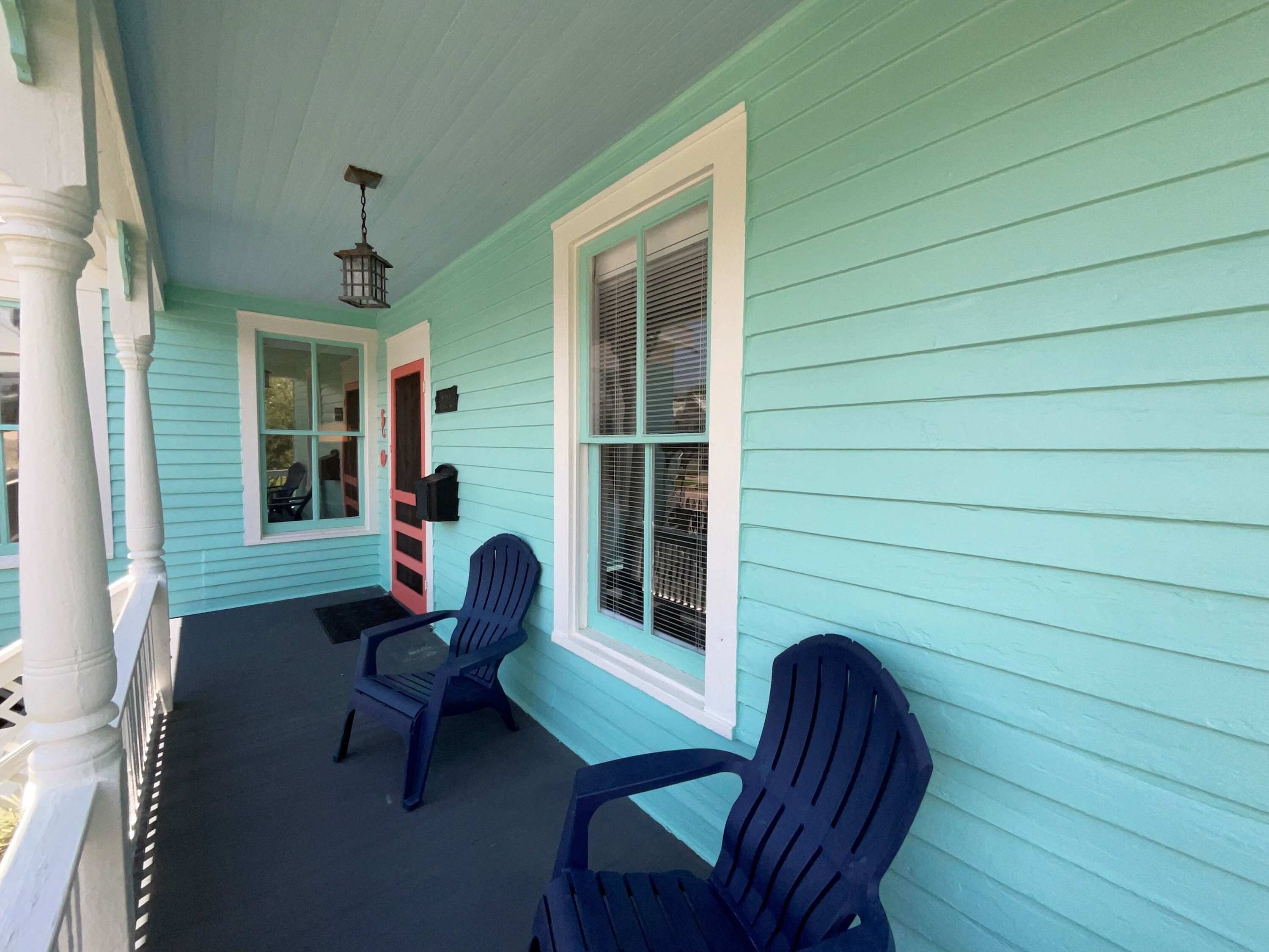 A porch with two Adirondack chairs, a mailbox, and a door with a red frame.