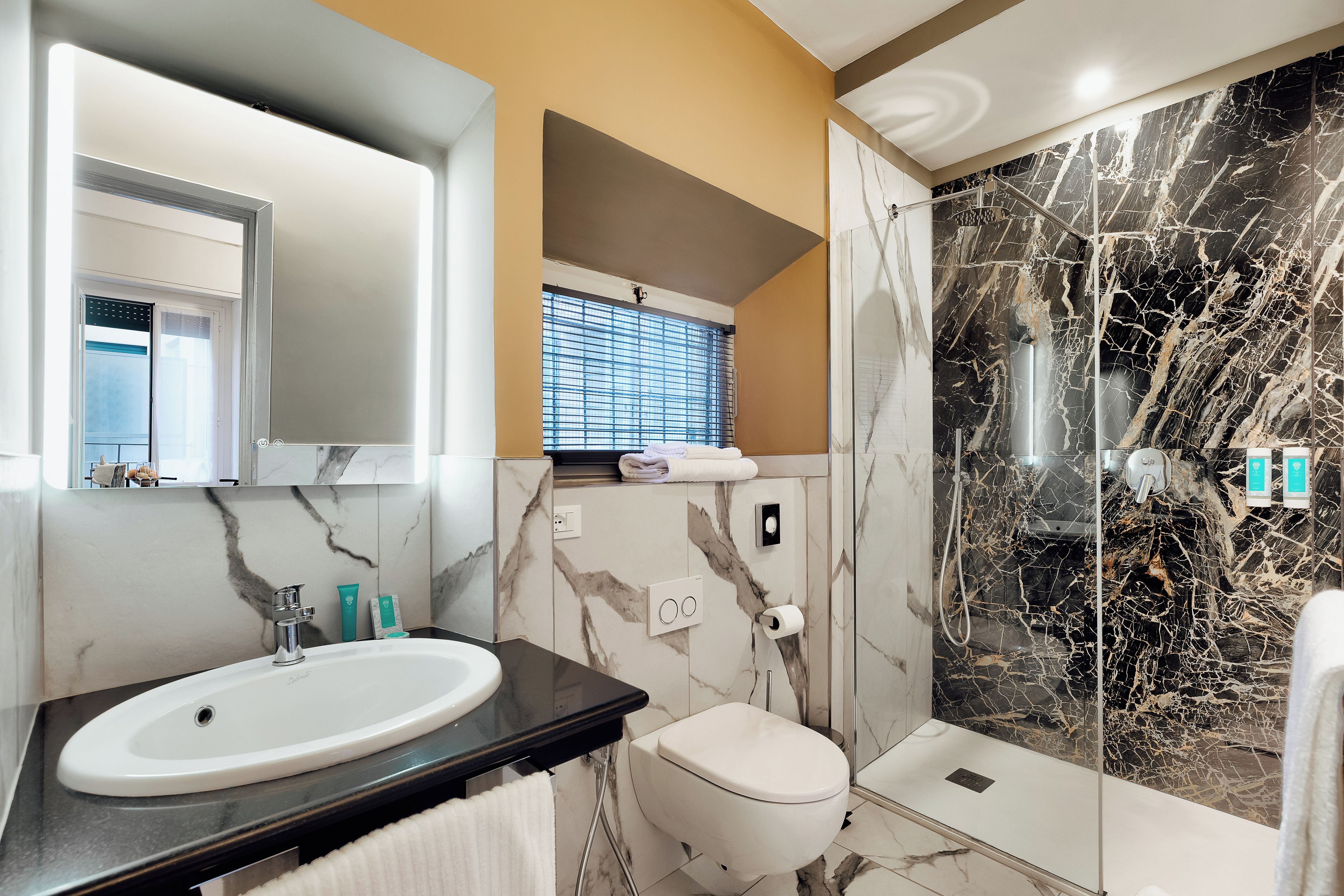 Une salle de bain avec un lavabo blanc, des toilettes et une douche avec un mur en marbre.