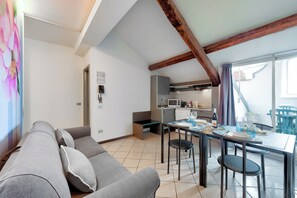 Una sala moderna con un sofá gris, una mesa de comedor preparada para dos personas y una cocina al fondo.