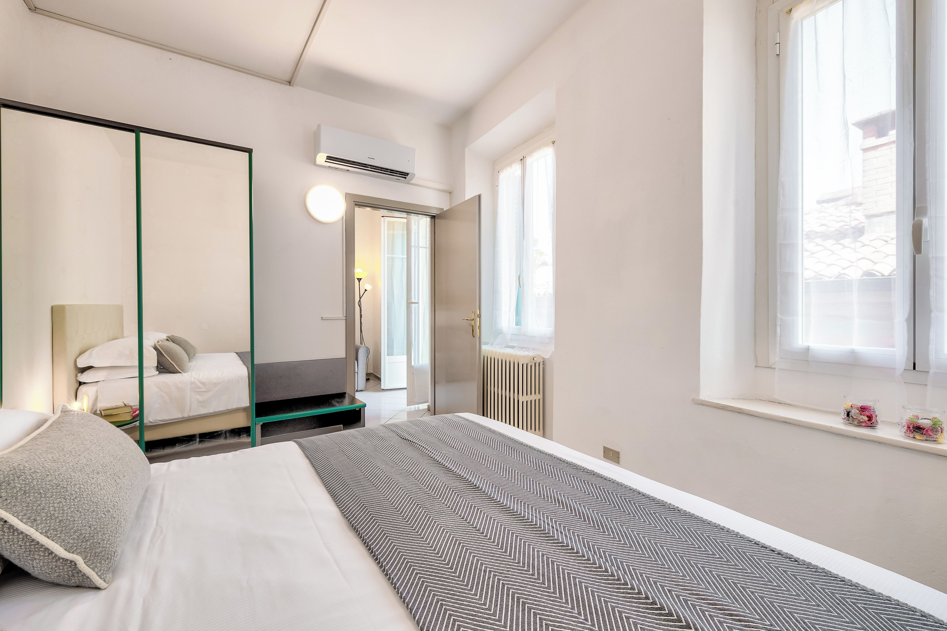 Ein Hotelzimmer mit Bett, Nachttisch, Spiegel, Heizkörper und einem Fenster mit Vorhängen.