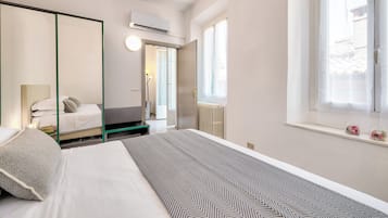 Ein Hotelzimmer mit Bett, Nachttisch, Spiegel, Heizkörper und einem Fenster mit Vorhängen.