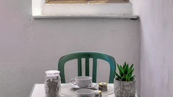 Une table placée devant une fenêtre donnant sur la mer, une chaise verte et une plante en pot.