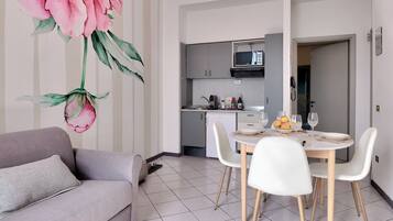Une cuisine moderne équipée d’un four à micro-ondes, d’un réfrigérateur et d’un coin repas avec des chaises et une table blanches.