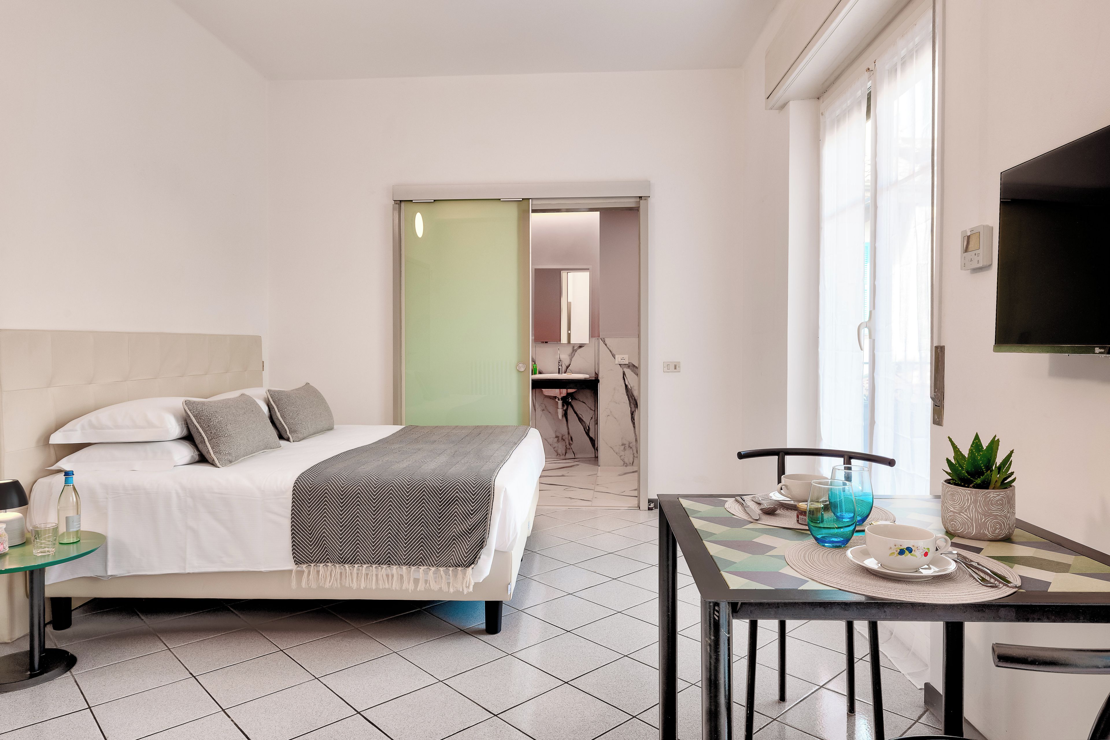 Habitación de hotel con cama, mesita de noche y un área de comedor con mesa y sillas.