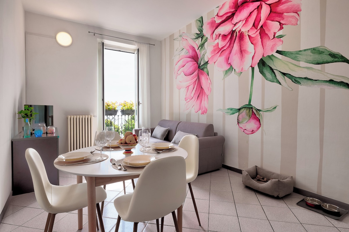 Un comedor con una mesa dispuesta para cuatro personas, sillas, un sofá y un gran mural floral en la pared.