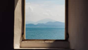 A window with a view of a calm sea and distant mountains.