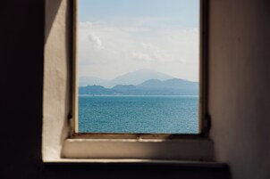 Una finestra vista su un mare calmo e montagne lontane.