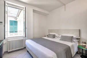 Una camera da letto con un letto, una finestra con persiane, un termosifone e un comodino con una lampada.