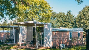 A small, single-story mobile home with a covered patio area, a brick exterior, and a small garden. - Tiny Cottage 2+2 (Kaatsheuvel)