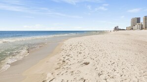 En strand med sand, vand og bygninger i baggrunden.