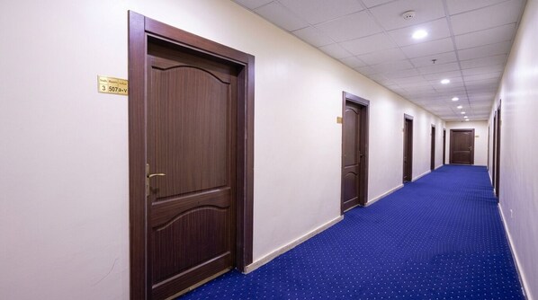 A hotel hallway with wooden doors, a blue carpet, and a ceiling with recessed lighting.