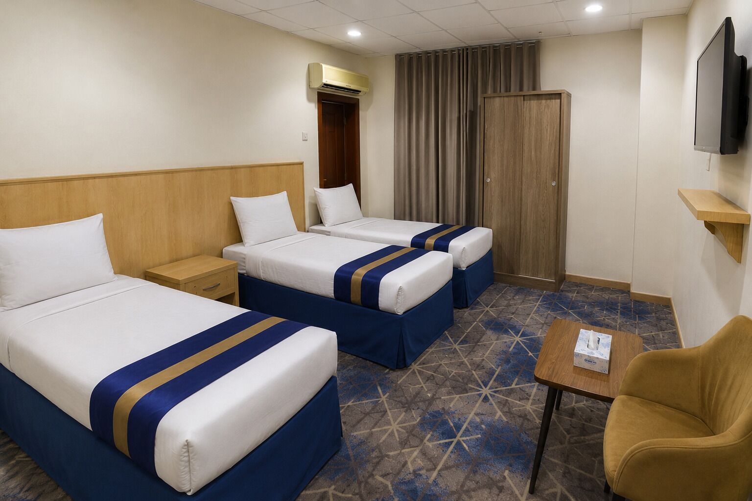 Une chambre d’hôtel avec deux lits, une petite table, une chaise, un téléviseur et un appareil de climatisation.