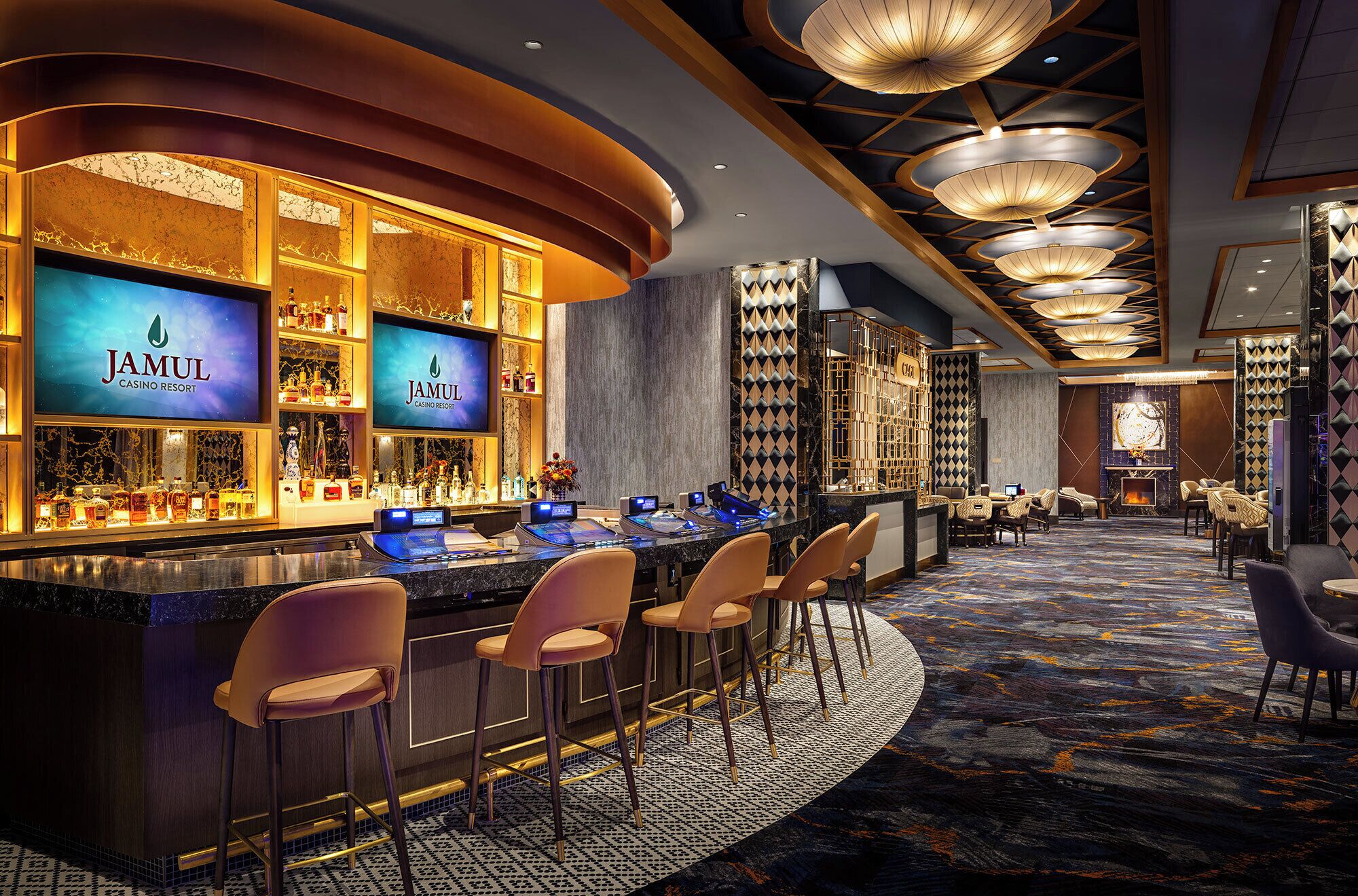 A bar area with multiple screens displaying the 'Jamul Casino Resort' logo, bar stools, and a patterned carpet.
