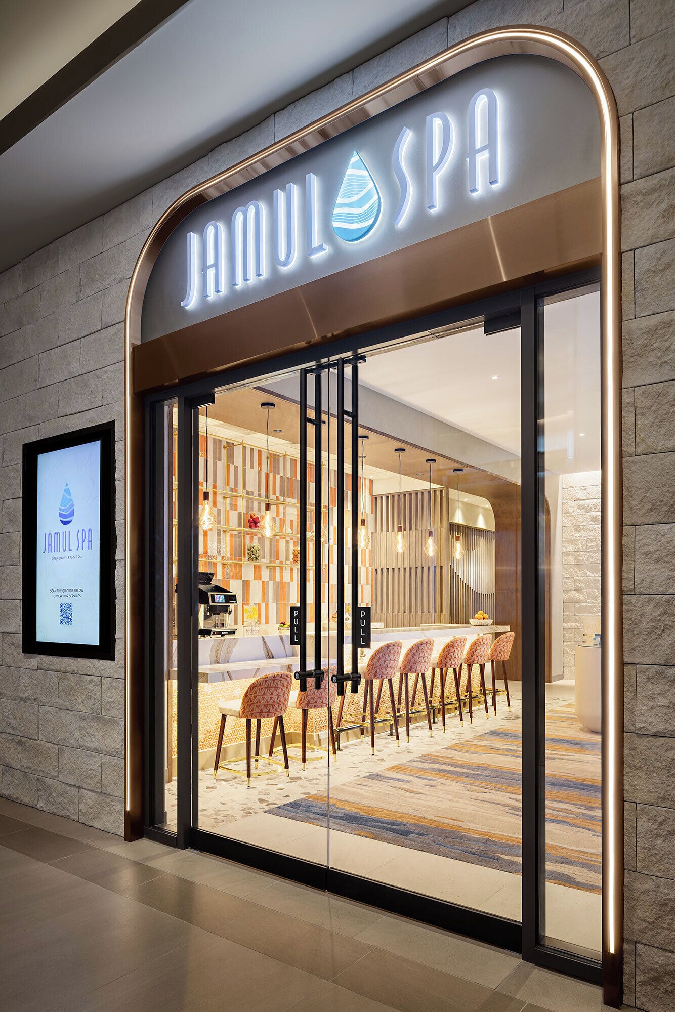 A spa entrance with a modern design, a reception desk, and a seating area visible through the glass doors.