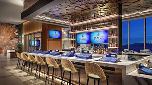Zona de bar con varias pantallas mostrando la marca 'Jamul Casino Resort', una variedad de botellas de licor y una fila de sillas de diseño único.