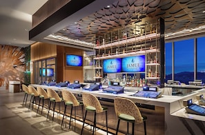 Un espace bar doté de plusieurs écrans diffusant des images de la marque « Jamul Casino Resort », une variété de bouteilles d’alcool et une rangée de chaises au design unique.
