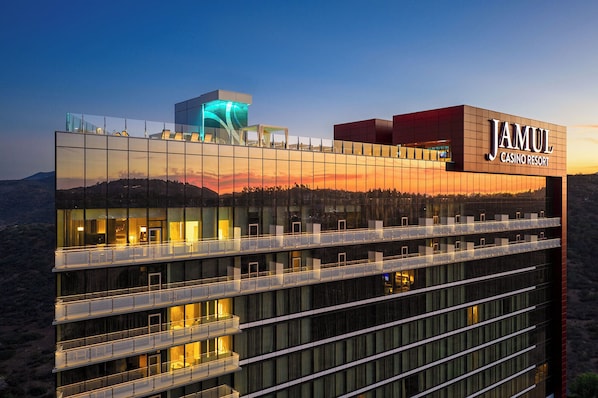 Un edificio moderno con fachada de vidrio reflectante, un llamativo letrero de 'JAMUL CASINO RESORT' y varios balcones.