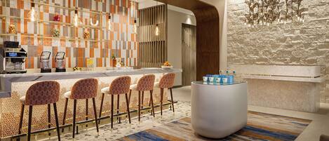 A modern bar area with a checkered tile backsplash, bar stools, a central bar counter, and a decorative light fixture.