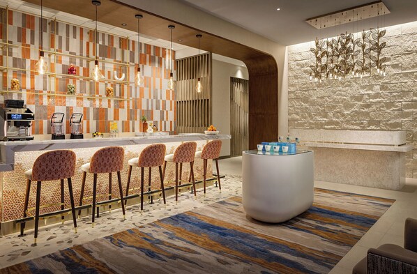 A modern bar area with a checkered tile backsplash, bar stools, a central bar counter, and a decorative light fixture.