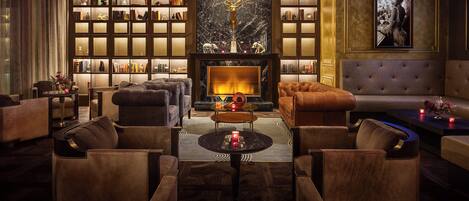 A luxurious lounge with leather sofas, a fireplace, bookshelves, and a chandelier.