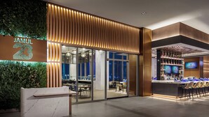 Exterior moderno de un hotel con área de bar, zona de estar con mesas y sillas, y un letrero iluminado grande.