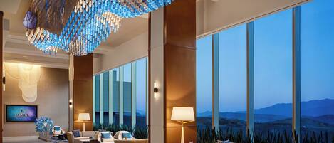 A hotel lobby with a modern chandelier, comfortable seating, a large window with a mountain view, and a television screen.