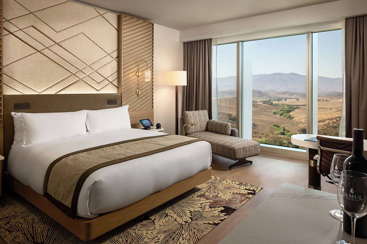 Habitación de hotel con una cama grande, una silla, una mesa y vistas a las montañas.