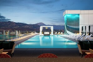 Un área de piscina con sillones de descanso, una zona de estar con cojines y vistas a montañas.