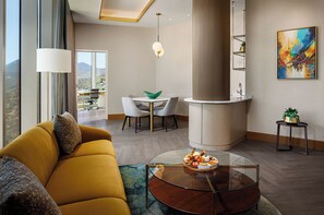 Una sala de estar moderna con sofá, una mesa de centro de vidrio con aperitivos, una zona de comedor con sillas, una isla de cocina y un ventanal con vistas.