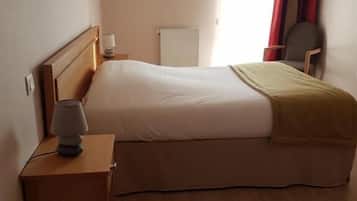 A hotel room with a bed, a nightstand, a lamp, a chair, and a window with curtains.