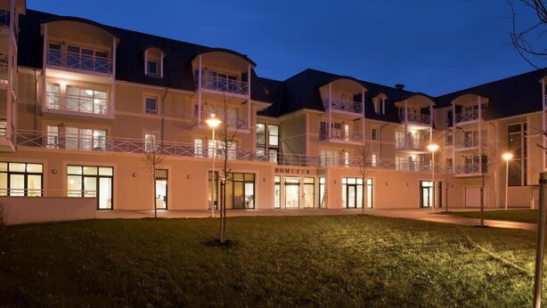 A multi-story hotel with balconies, a central courtyard, and a well-lit entrance. - Domitys - Le Carroussel (Cabourg)