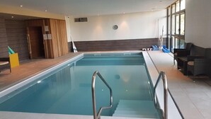 An indoor swimming pool with steps leading into it, a clock on the wall, and a seating area with chairs and a table. - Domitys - Le Carroussel (Cabourg)