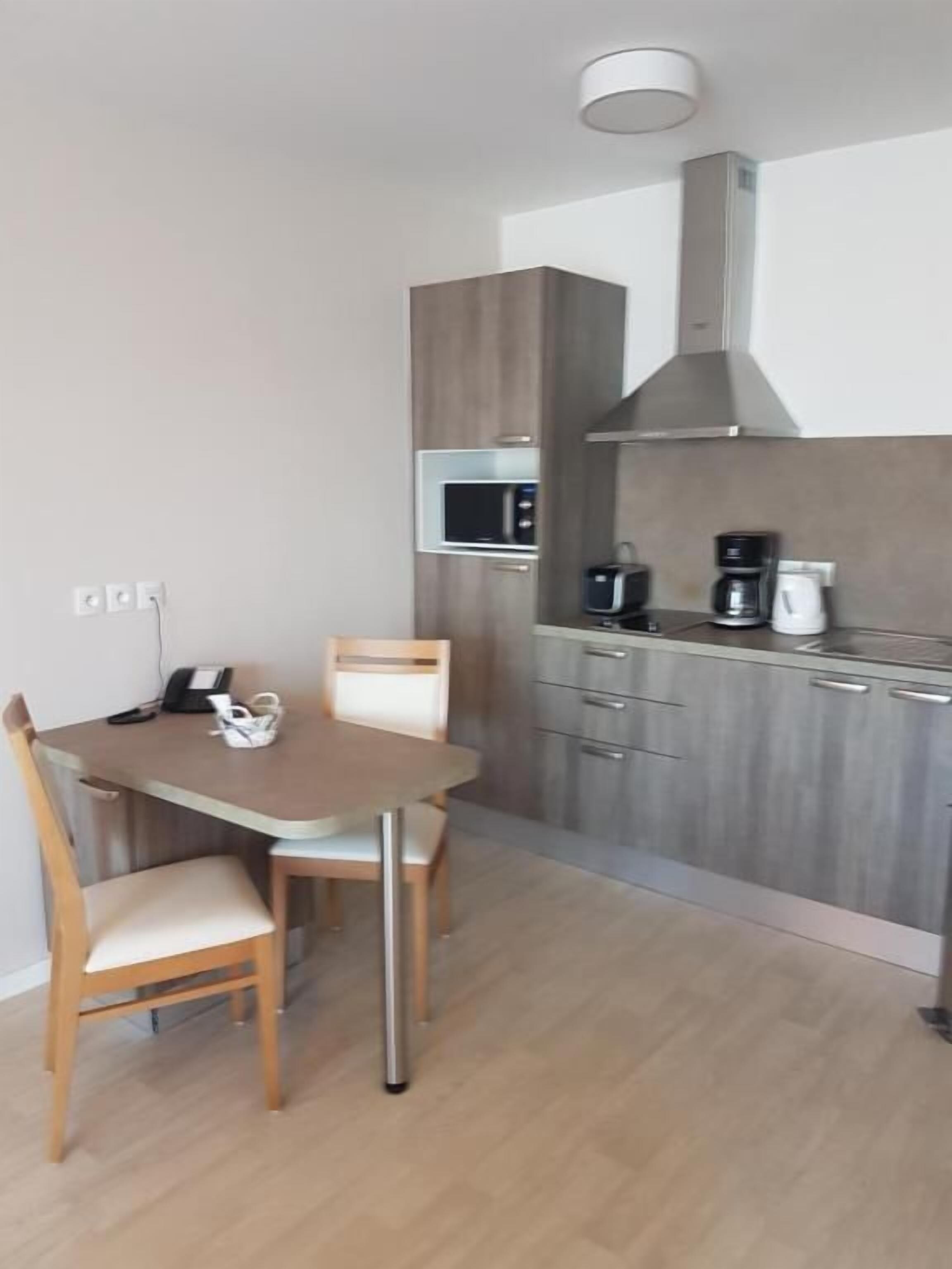 Een moderne keuken met een eettafel, stoelen, een magnetron en een koffiezetapparaat.