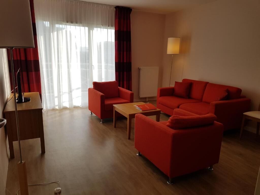 Ein Wohnzimmer mit einer Couch, Sesseln, einem Couchtisch, einer Lampe und einer Heizung.