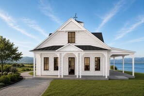 Ein weißes, eingeschossiges Haus mit Satteldach, einer Veranda und Blick auf einen See.