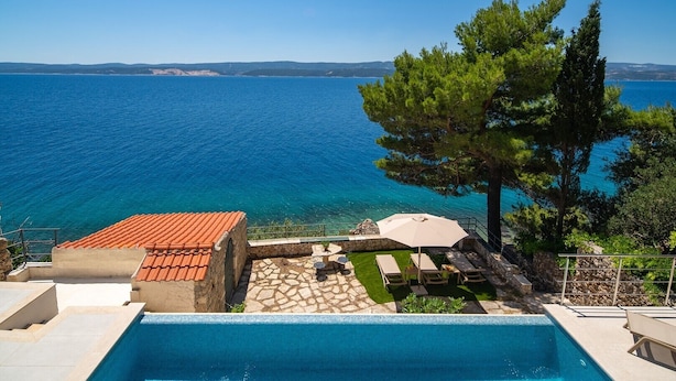 Ein Pool mit Meerblick, Sitzgelegenheiten im Freien und ein Steinhaus.