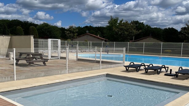 A rectangular swimming pool with a white fence, lounge chairs, and a tiled deck.