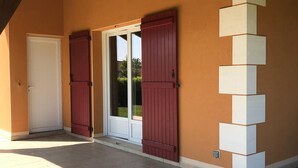 A covered outdoor area with a door, red shutters, and a tiled floor.