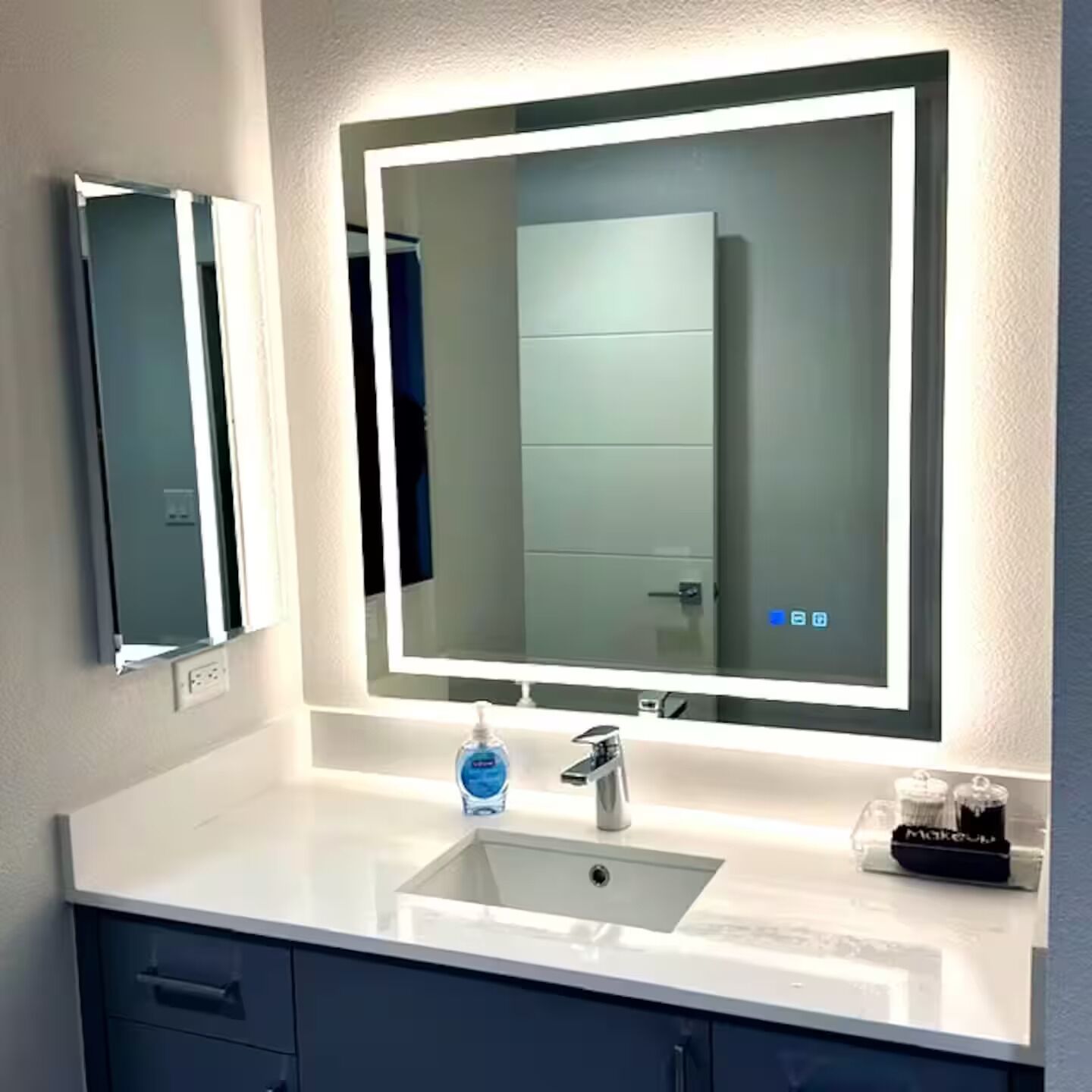 A bathroom with a large mirror, a sink, and a bottle of hand soap.