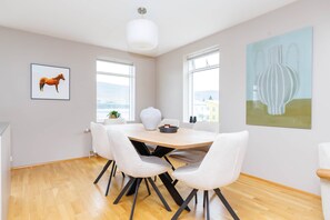 A dining area with a round table, white chairs, a white vase, and a painting of a horse.