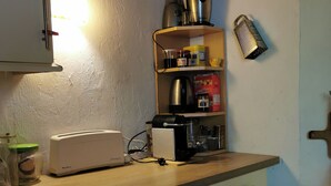 A kitchen with a toaster, a blender, and a coffee maker on the counter. There is a shelf with jars and a box of cereal. - Small house with a garden in the heart of Old Antibes (Antibes)