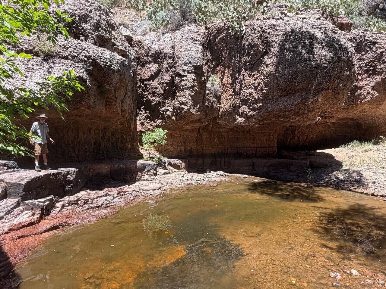 A natural landscape with a rocky cliff, a small pool of water, and a person standing on a rock.