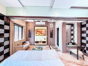 Quarto com cama, sofá, televisão e banheiro visível por uma porta aberta.