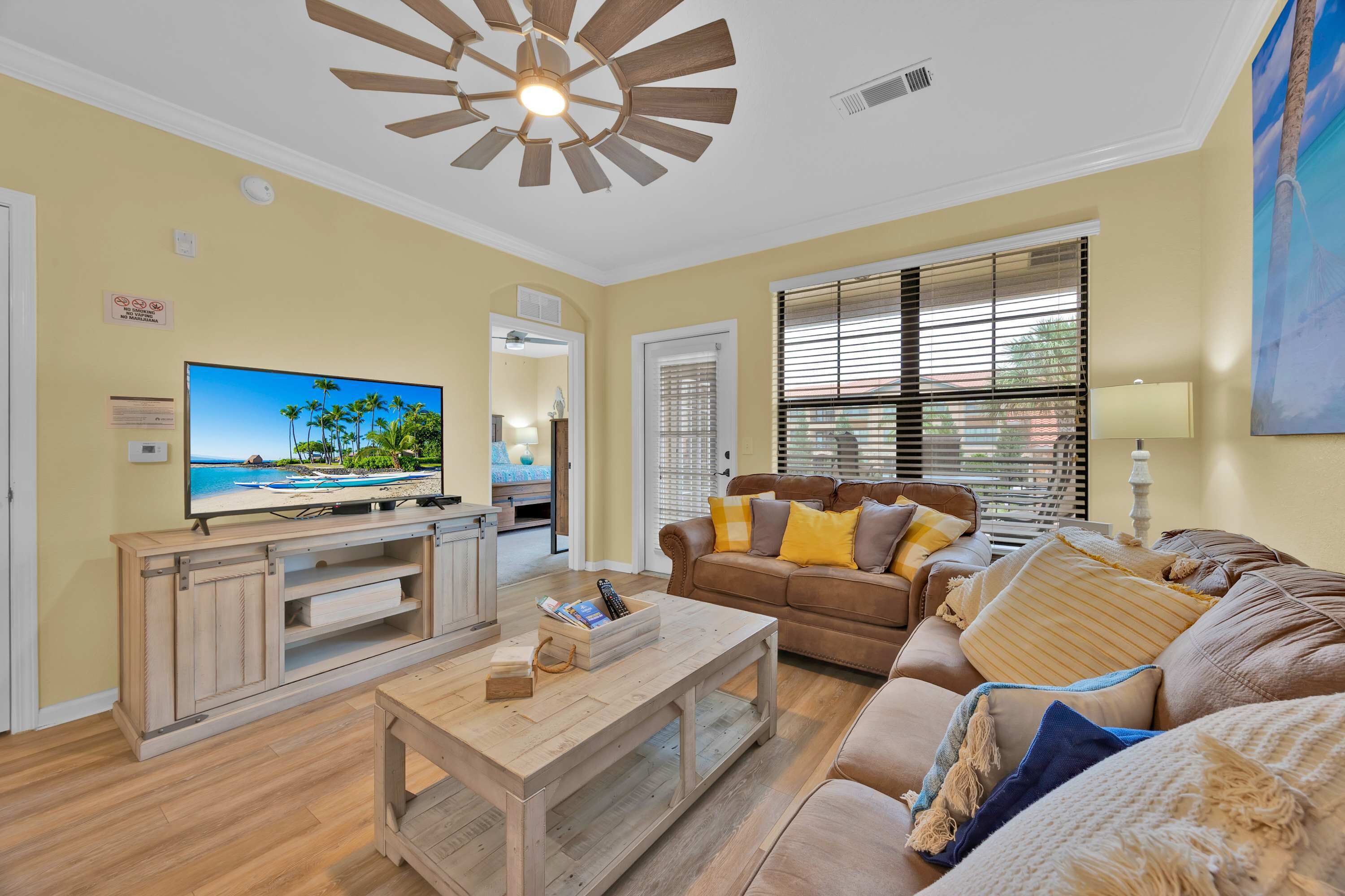 Sala de estar con televisor, mueble de madera para entretenimiento, sofá de cuero marrón y ventilador de techo.